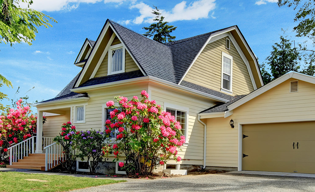 Pink flowers bloom in front of a home with pale yellow exterior paint. 
