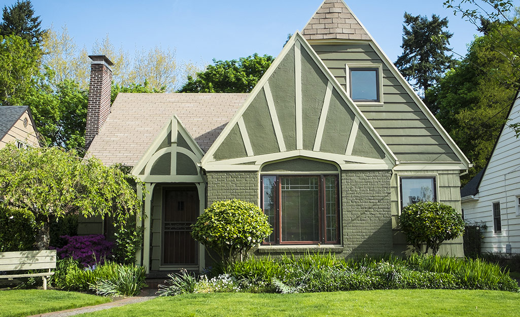 An earthy green cottage blends in with the trees and bushes around it.