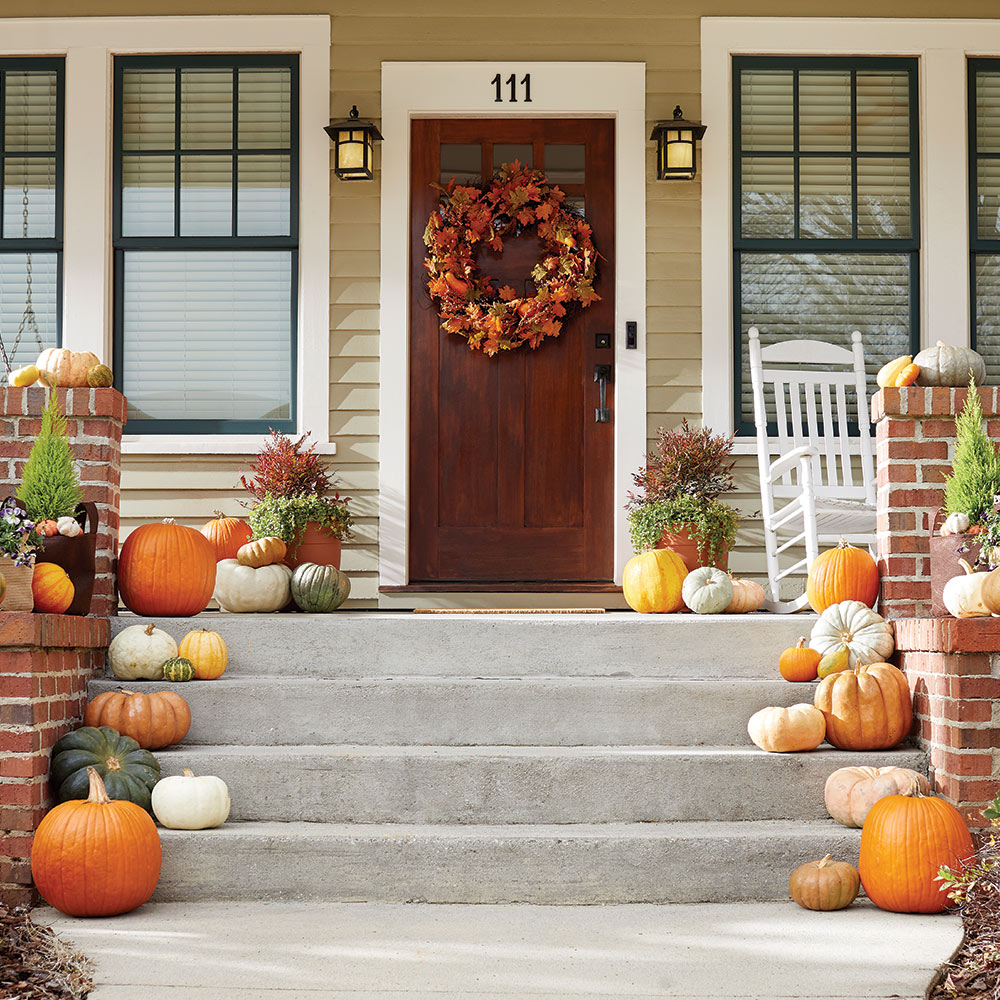 Pumpkins line the steps up to a front porch decorated for fall.