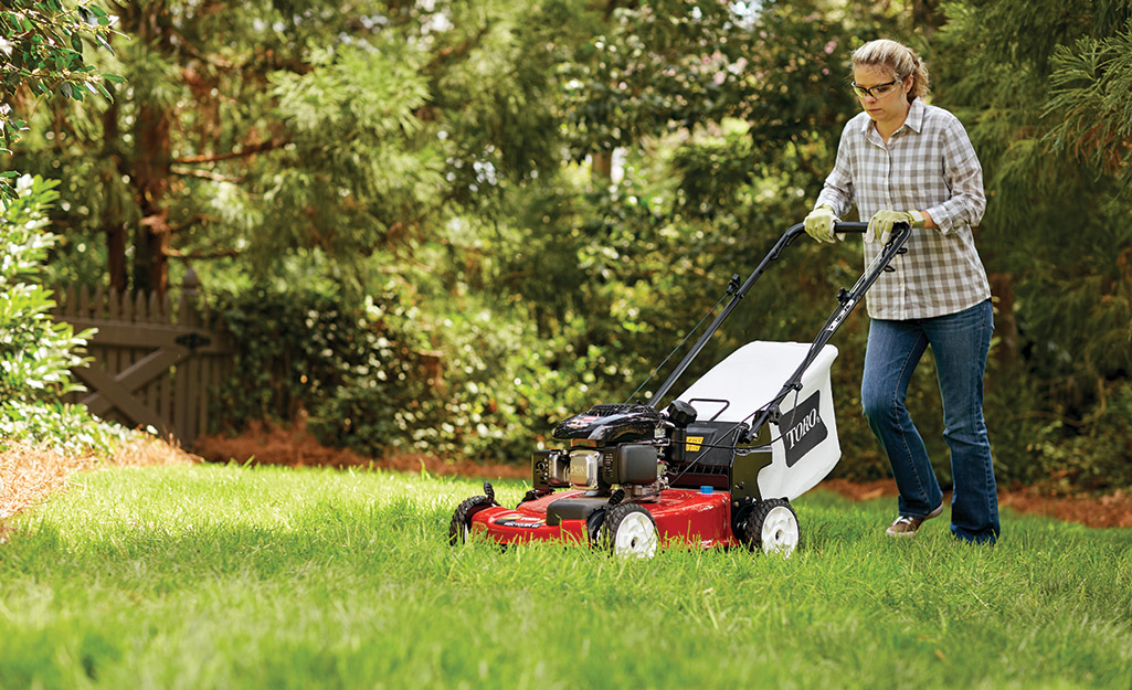 A woman mows a lawn as part of fall lawn care prep.