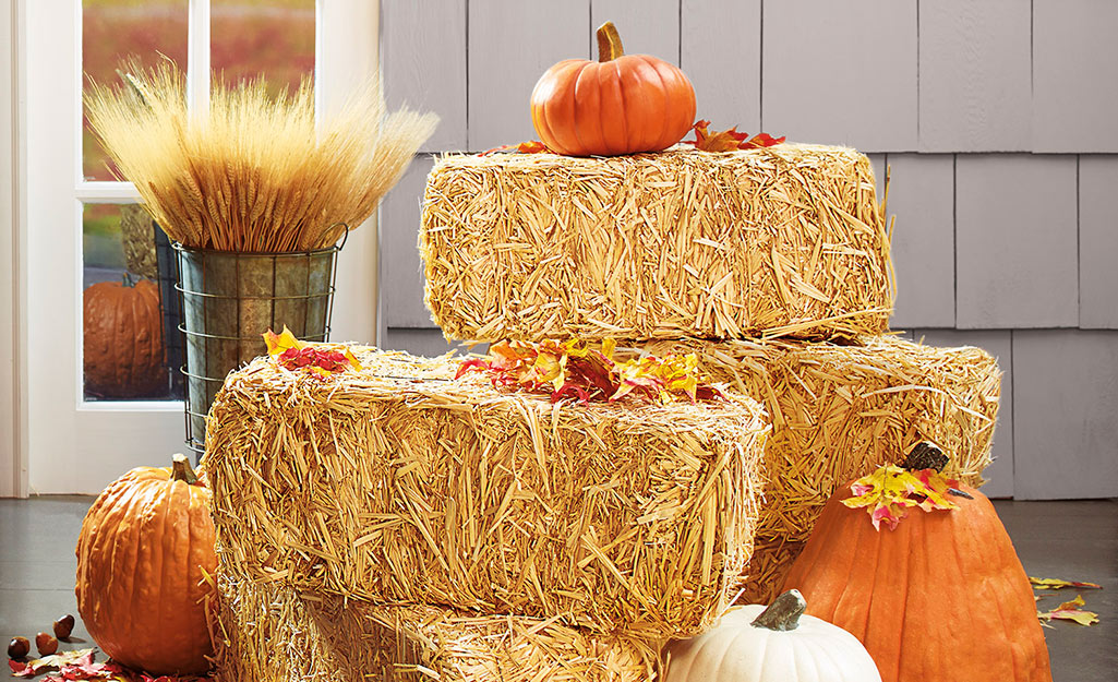 A fall porch decorated with pumpkins and straw bales.