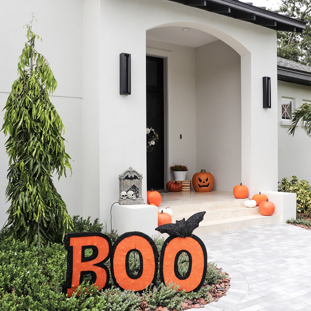 A white home with black accents is decorated with an Boo sign for Halloween.