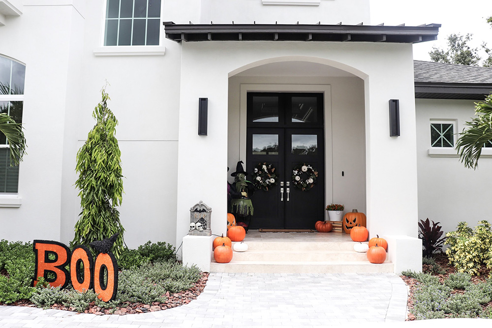 A home with black double doors is decorated with orange pumpkins for Halloween.