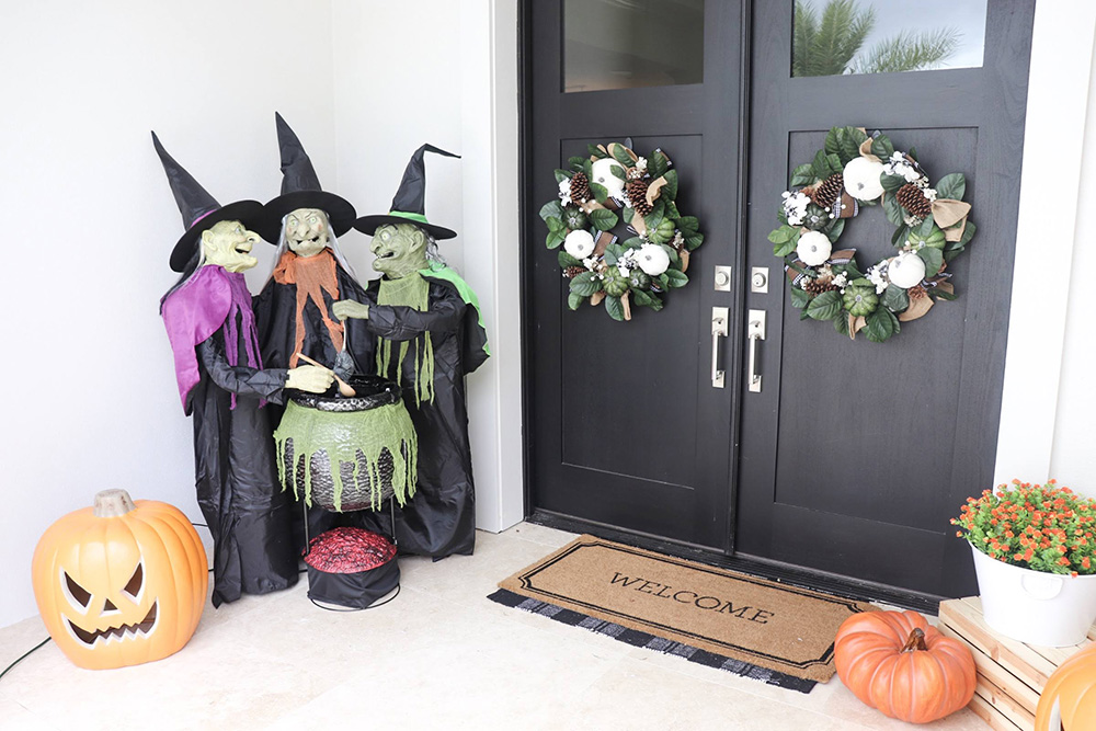 A front porch decorated for Halloween with pumpkins and a trio of witches.