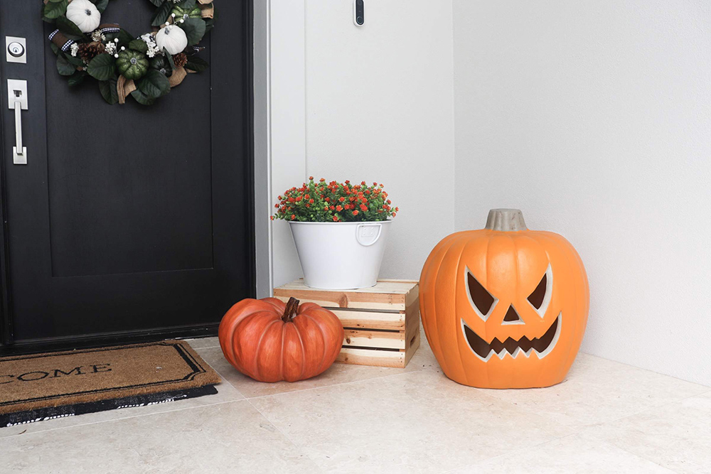 The corner of a porch decorated with a pumpkin, spooky Jack-O-Lantern, and a white planter with flowers.