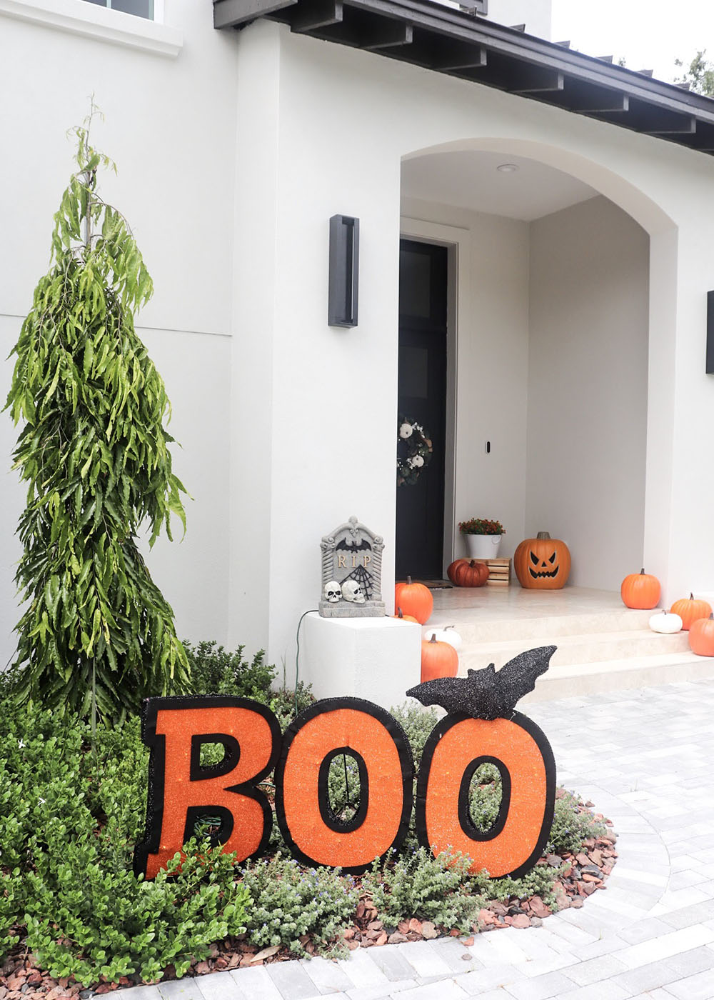 A pathway leading to a front door with a large orange and black Boo sign with a bat on top.