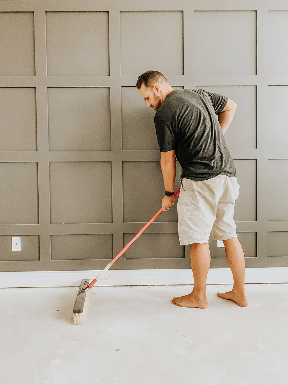 A man pushing a broom on concrete floors.