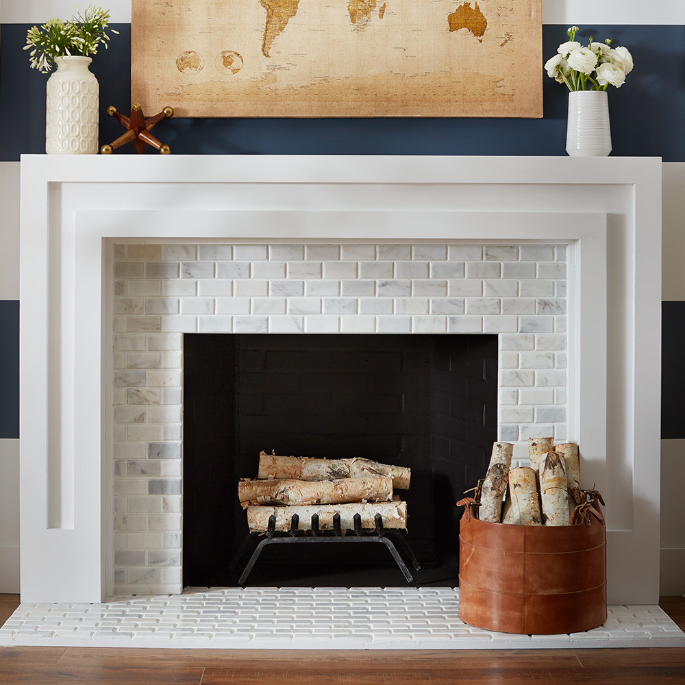 A white brick fireplace with firewood stacked on a grate and a basket of more firewood sitting on the hearth.