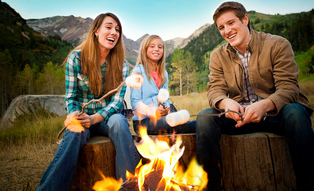 A man, woman and young girl roasting marshmallows over an outdoor campfire.