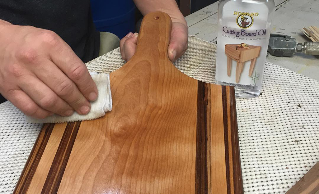 A person rubs a wood surface with a cloth and food-safe mineral oil.
