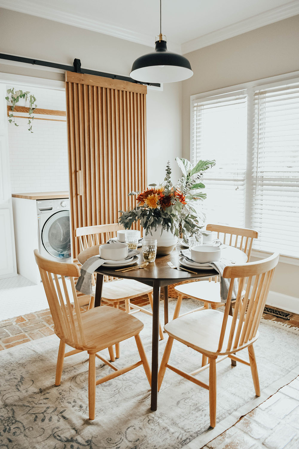 A round small table with four wooden chairs decorated with a floral arrangement and place settings.