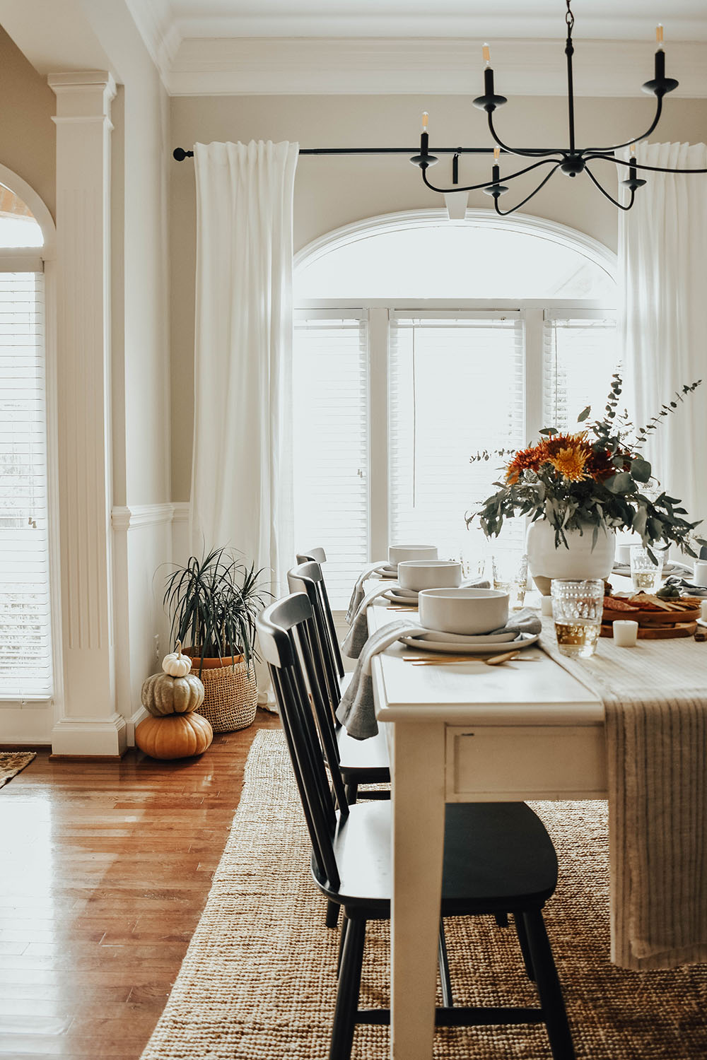 A dining room decorated with a large rug, dining table, and pumpkins with greenery.