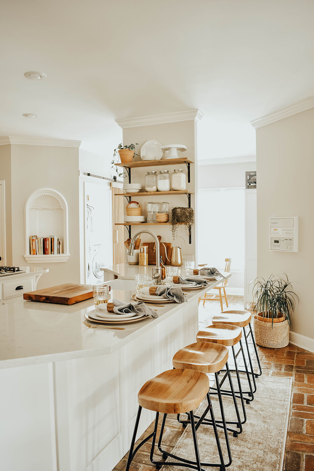 A kitchen with open shelving, black and wooden barstools, and place settings on an island.