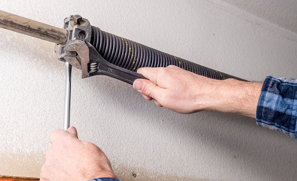 A person uses a wrench to adjust a garage door spring.