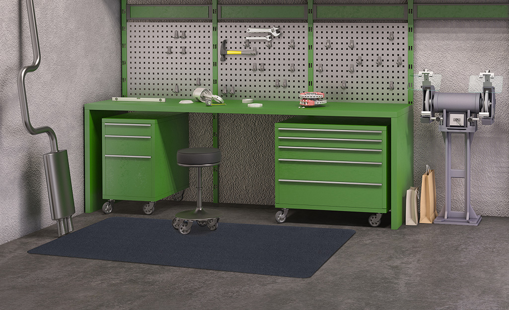 A garage flooring mat lays in front of a workbench and green storage drawers.