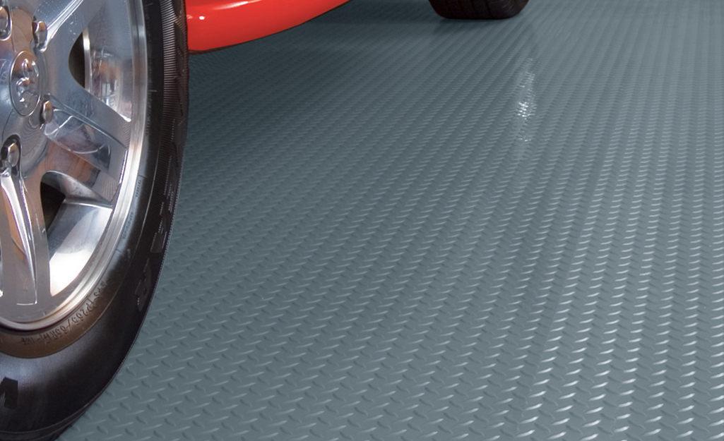 A car parks on a garage flooring mat with raised coin-shaped patterns.