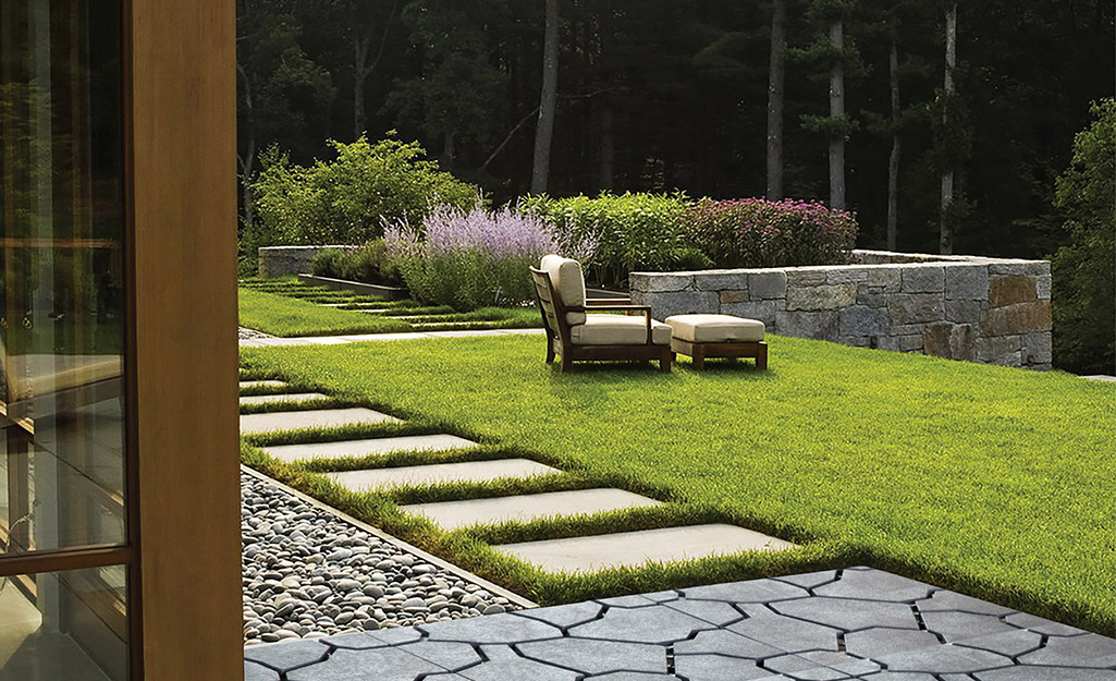 A paver path through a backyard of grass to a garden.