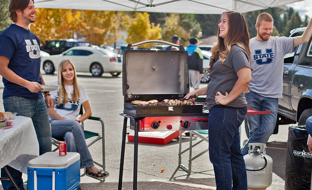 A person cooks food on a portable propane gas grill at a tailgate party.