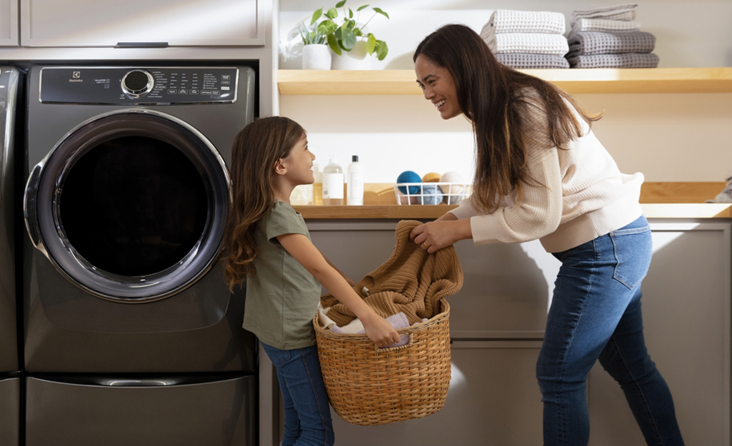 A child helps mom add clothes to a washer and dryer in a laundry room.