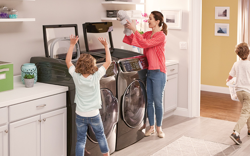 A child helps his mother add clothes to a washer and dryer in a laundry room.
