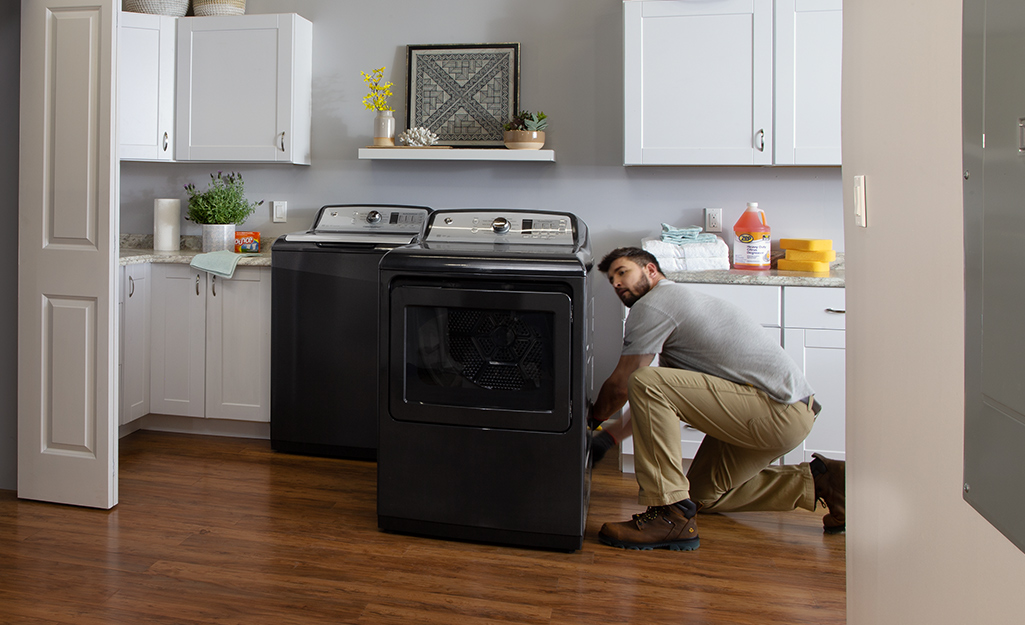 A man kneels down to install a new washing machine and dryer in a laundry room.
