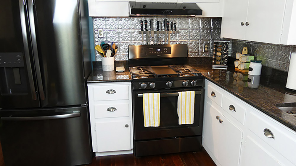 The corner of a kitchen with a GE black stainless steel gas range and under the cabinet range hood.
