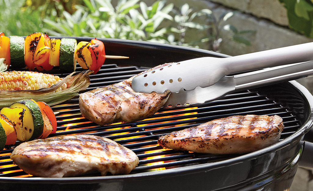 A person uses tongs to flip their grilled chicken. 
