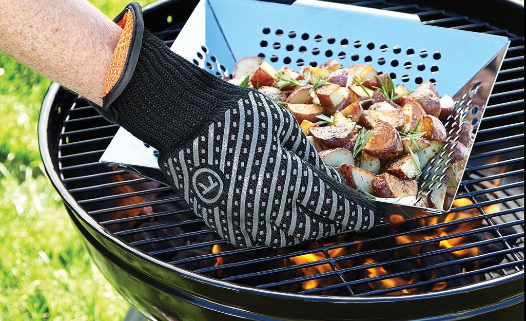 A person wears grilling gloves when using a charcoal grill.
