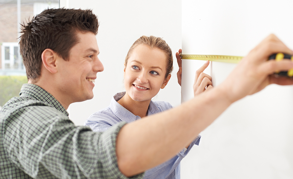 A couple measuring the length of a wall with a measuring tape. A couple measuring the length of a wall with a measuring tape.