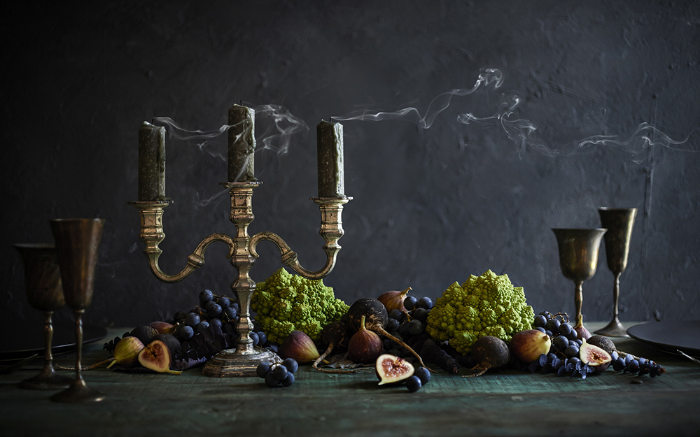A table with black candles and fruit on top.
