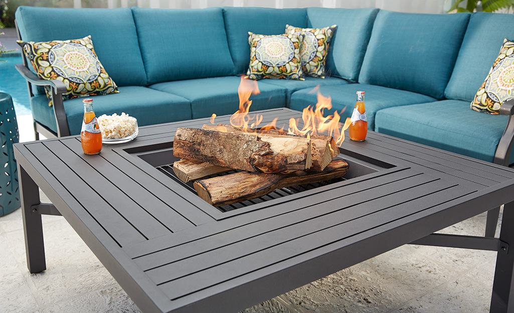 A Hampton Bay patio sofa set with blue cushions and a brown patio table with a built-in fire pit.