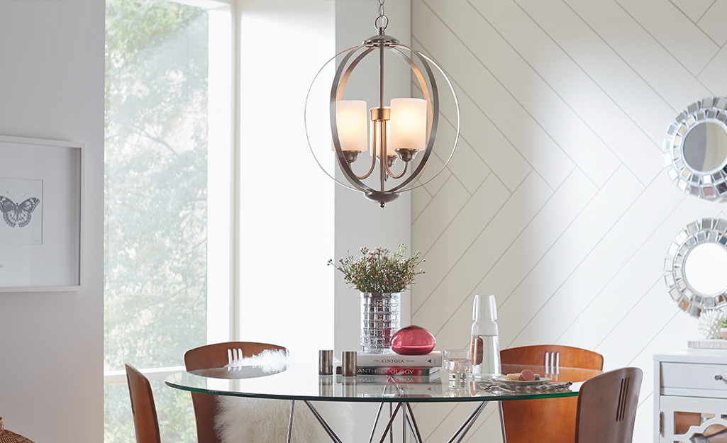 A Hampton Bay chandelier lighting fixture over a glass-topped table with chairs. 