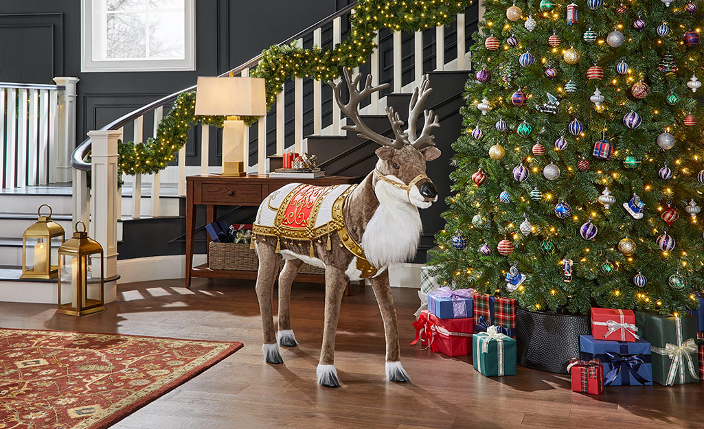 An animatronic reindeer stands near a decorated Christmas tree and a staircase.