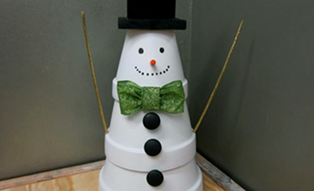 A stack of terra cotta pots painted and decorated to look like a snowman.