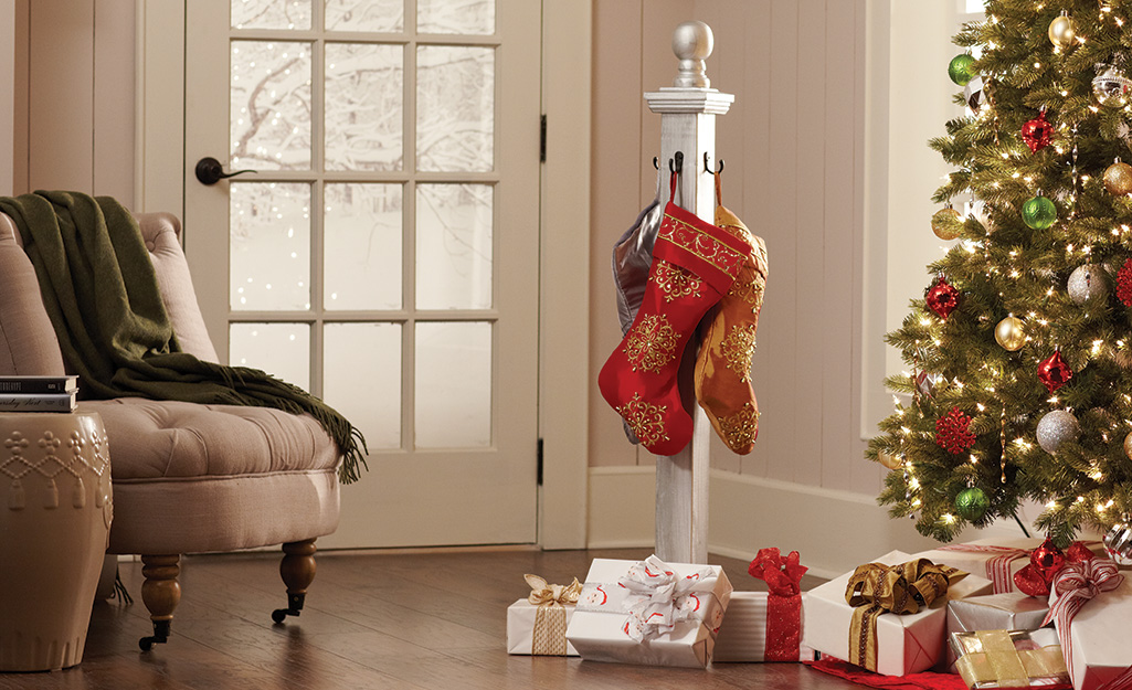 Stockings hang from hooks on a wooden pole over a pile of wrapped presents next to a decorated Christmas tree.