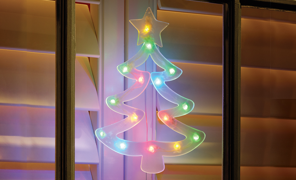 A multicolor lighted Christmas tree window cling attached to the outside of a window pane.