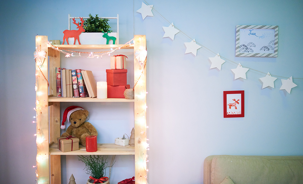 A bookshelf decorated with small holiday decorations and mini string lights.