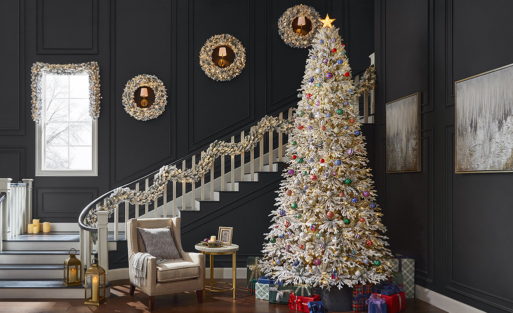 A white Christmas tree next to a staircase with white garland and white wreaths on the walls