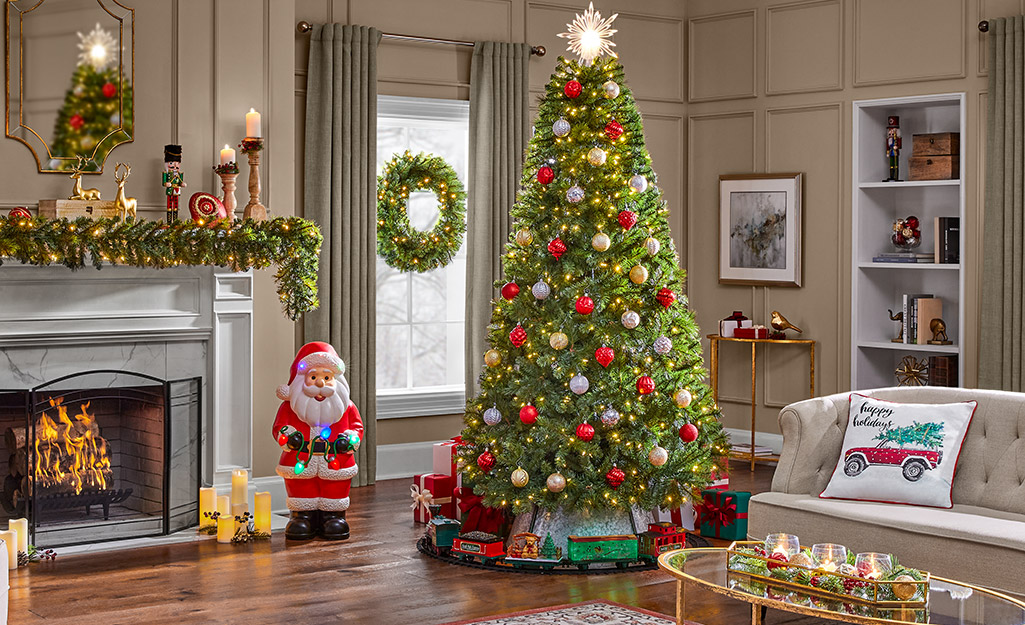 A Christmas tree with a train running around it stands in the corner of a living room decorated in a retro holiday style.