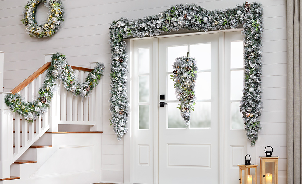 Silver and green garlands hang over a doorway and on staircase rail in a house's white entranceway.