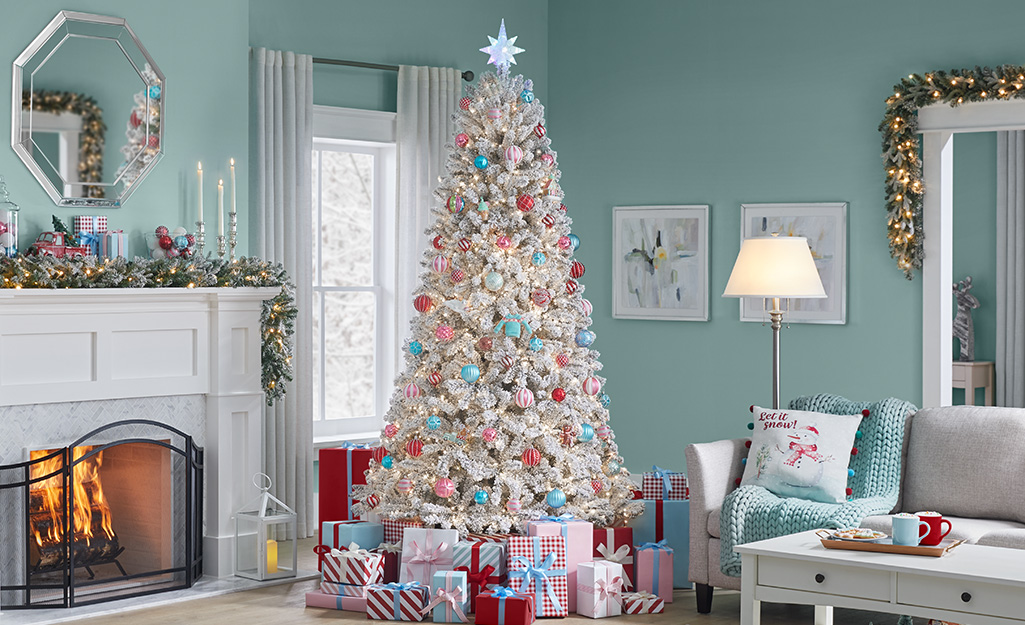 A white Christmas decorated in red and turquoise stands in the corner of a room with a lit fireplace.