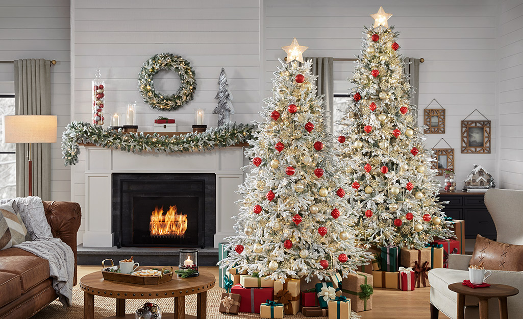 Two Christmas trees stand next to a lit fireplace in a room with a shiplap wall.