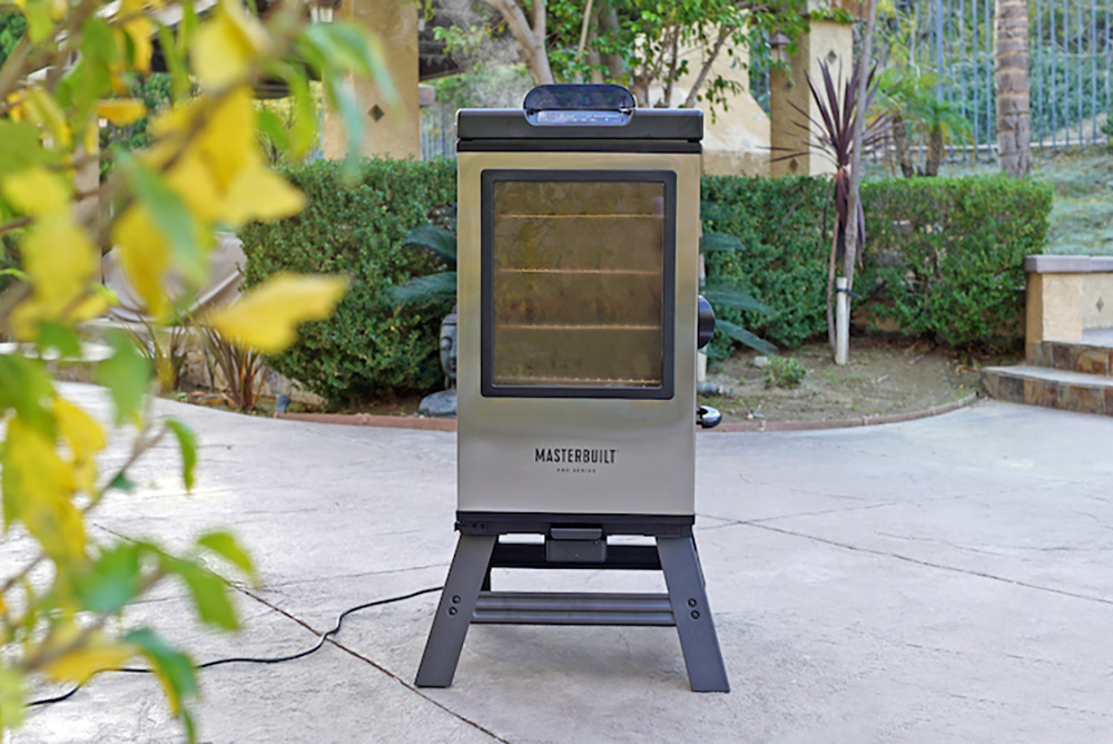 A Masterbuilt Electric Smoker sitting outside in front of bushes.