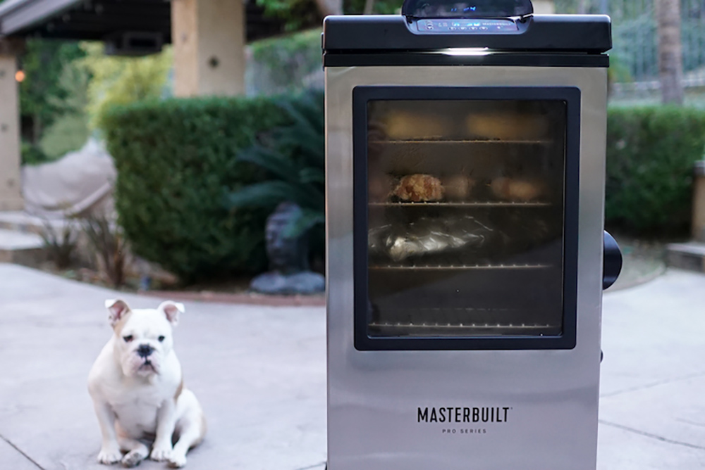 A dog sitting in the background while food is smoked inside a Masterbuilt Electric Smoker.