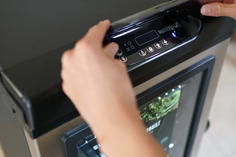 A person touching an LED digital control panel display on a Masterbuilt electric smoker.