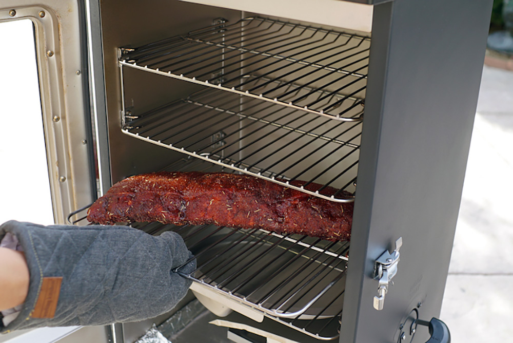 A person adding meat inside a smoker.