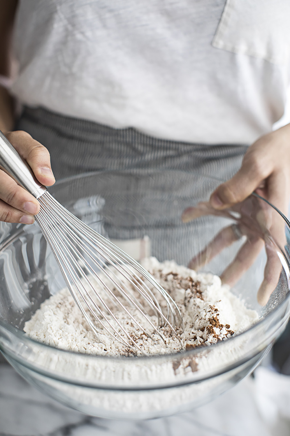 A person using a whisk to combine the dry ingredients in a glass bowl.