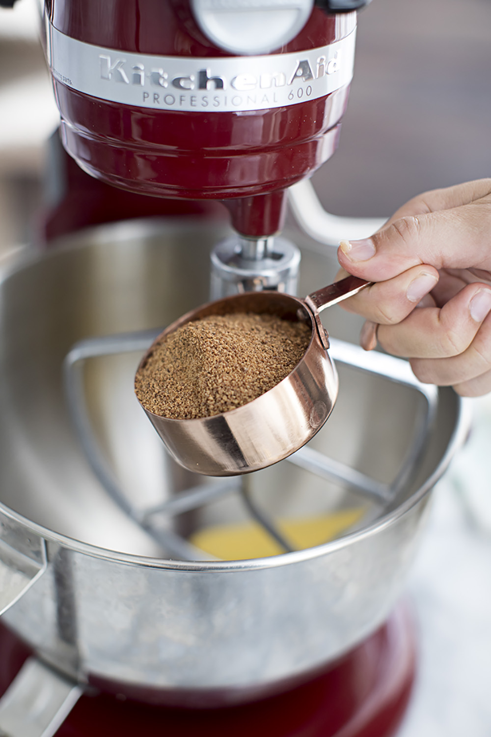 A person adding brown sugar to a stainless steel mixer.