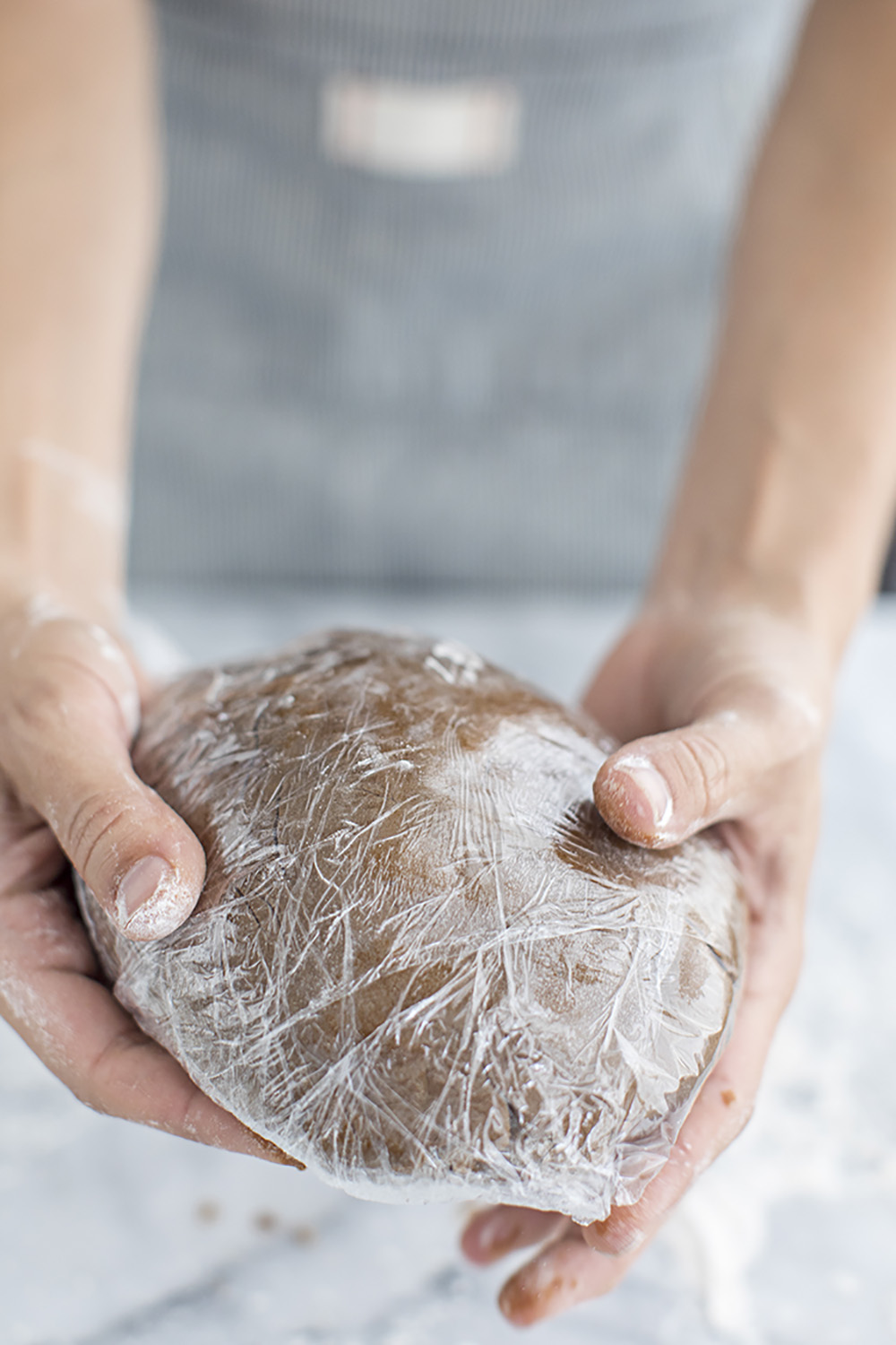 A person holding gingerbread cookie dough wrapped in plastic wrap.
