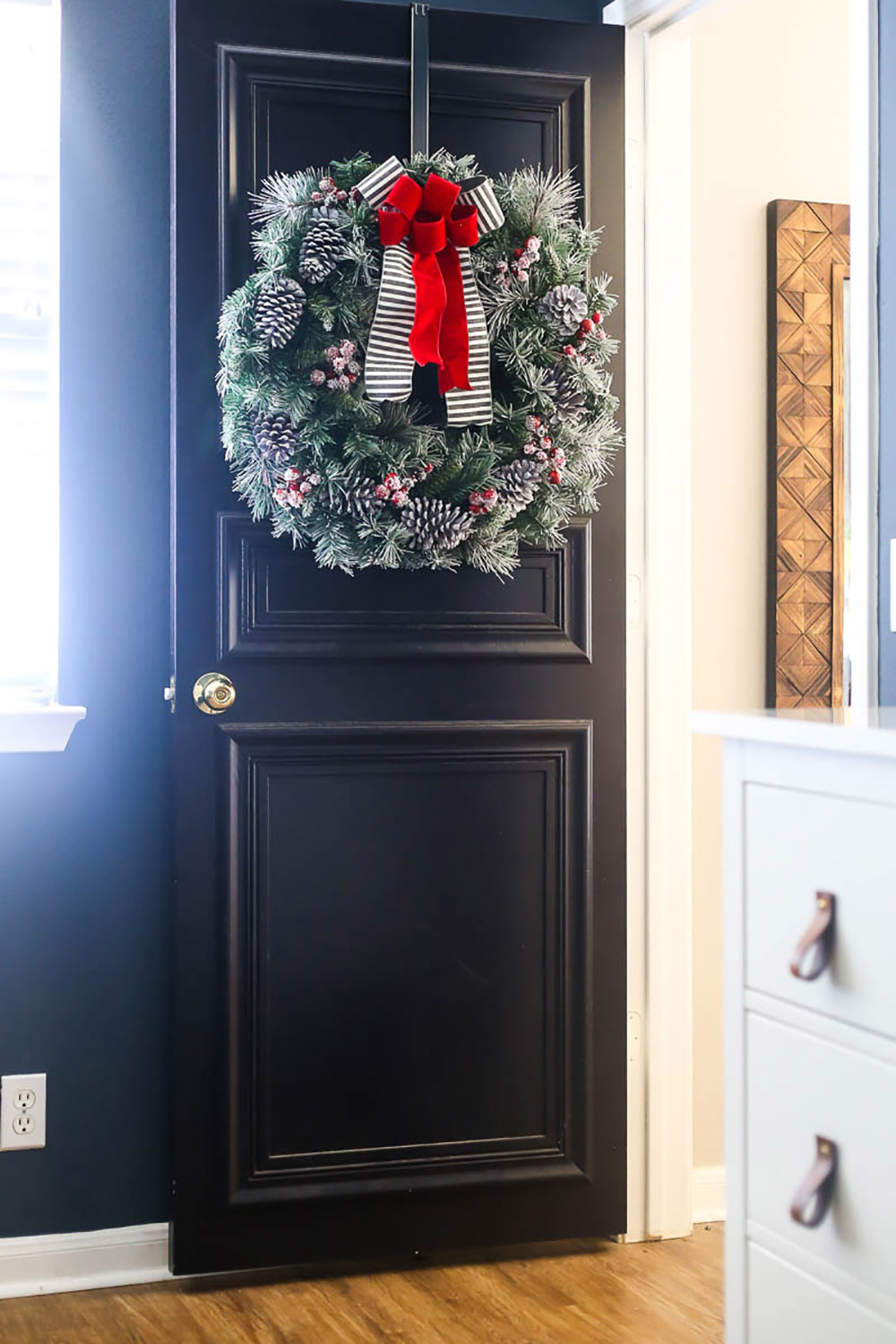 A large wreath with pinecones, berries, and bows hangs on a black bedroom door.